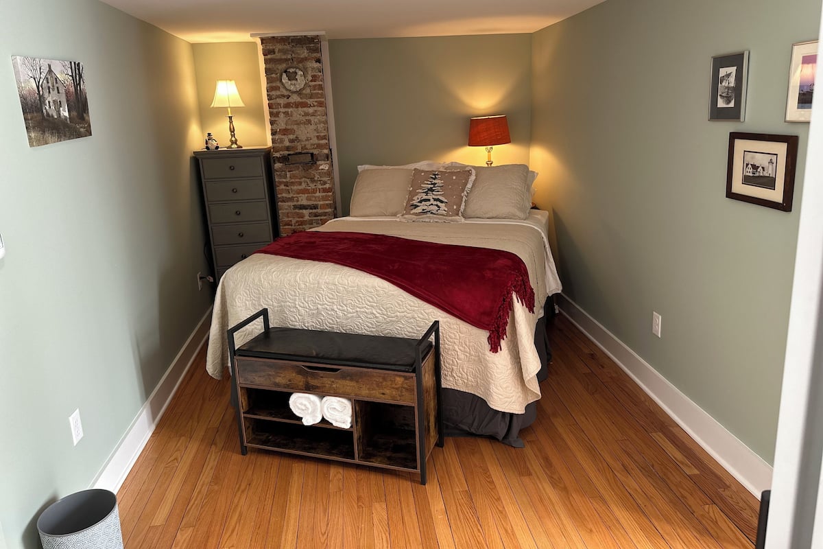 A bedroom with a bed, a dresser, a nightstand, a lamp, a wall clock, and a small table with towels.