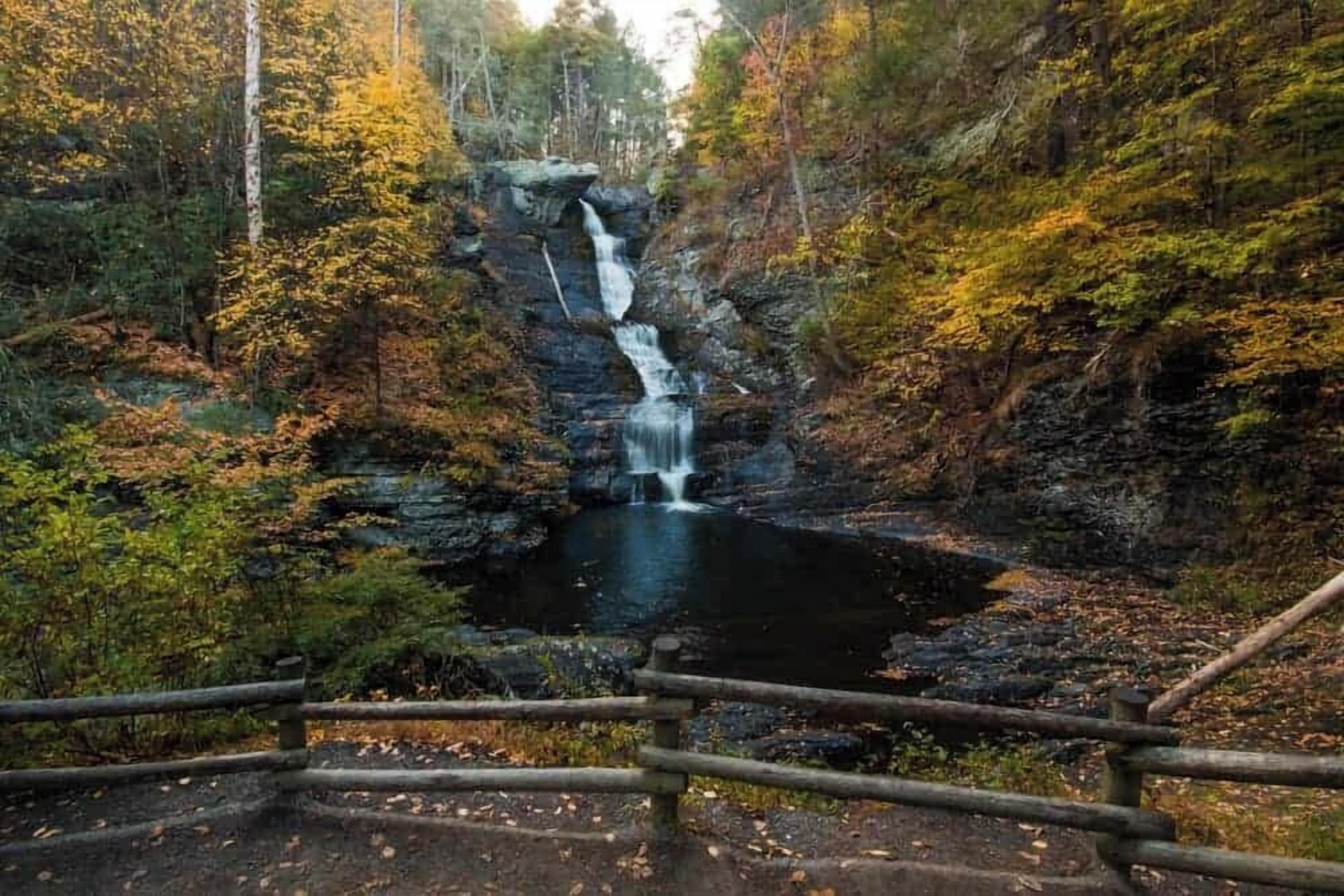 Ein Wasserfall in einem bewaldeten Gebiet mit einem Holzzaun im Vordergrund.