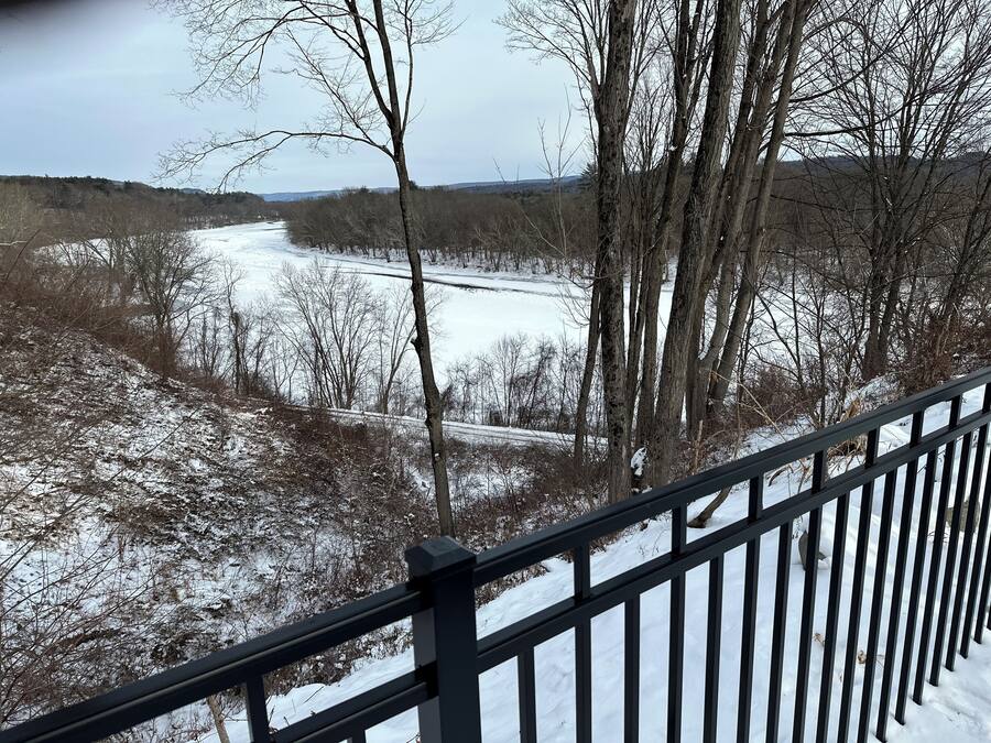 A snowy landscape with a river, trees, and a metal railing.