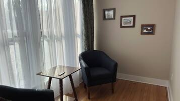 Una habitación con un sillón azul oscuro, una pequeña mesa de madera y un sofá. Hay tres cuadros enmarcados en la pared.