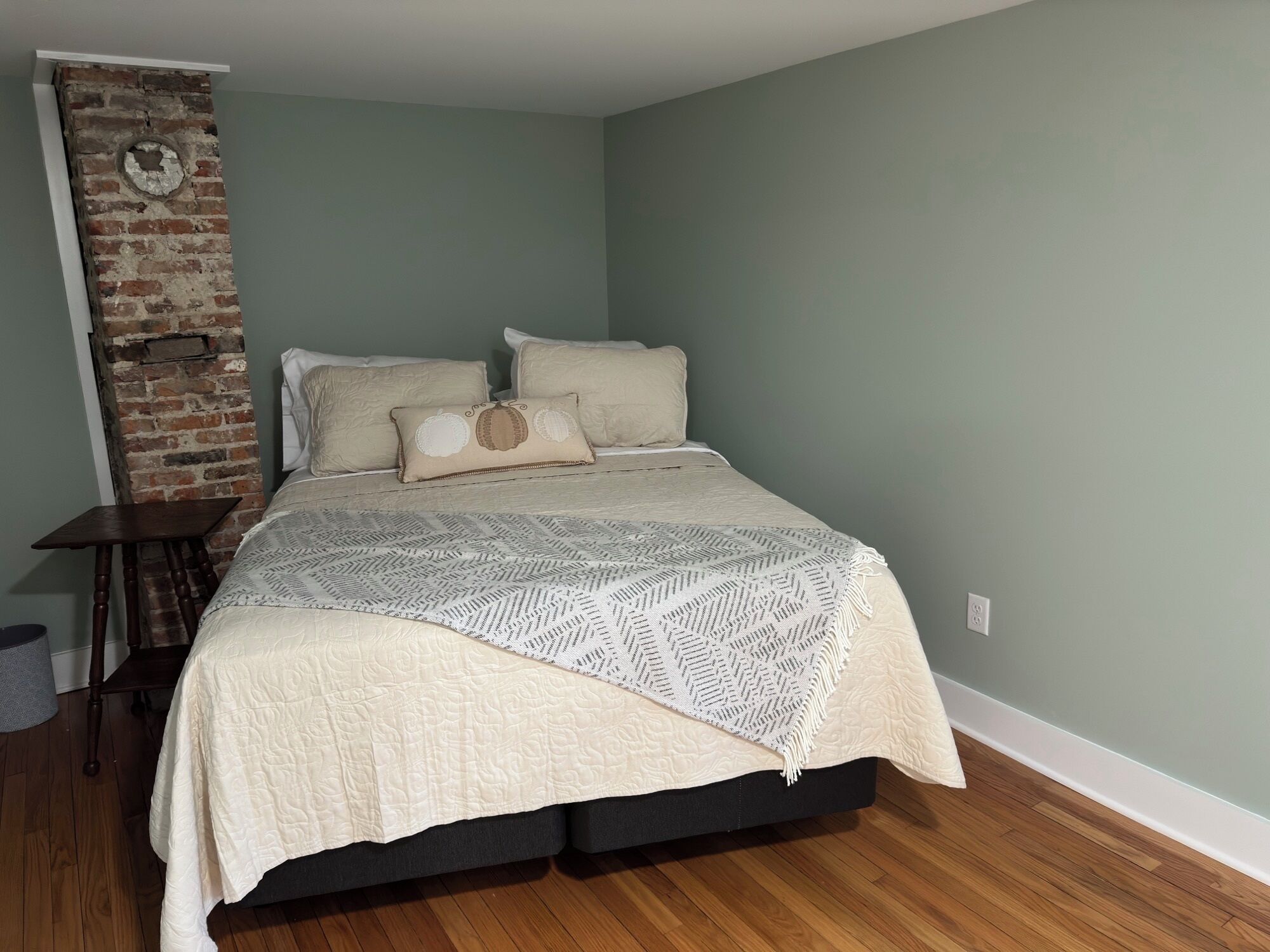 A bedroom with a bed, a wooden nightstand, a brick accent wall, and a small table.