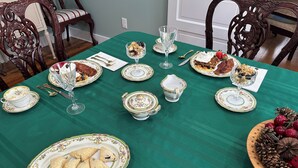 Una mesa de comedor adornada con platos ornamentales, cubiertos y cristalería, rodeada de sillas de estilo antiguo.