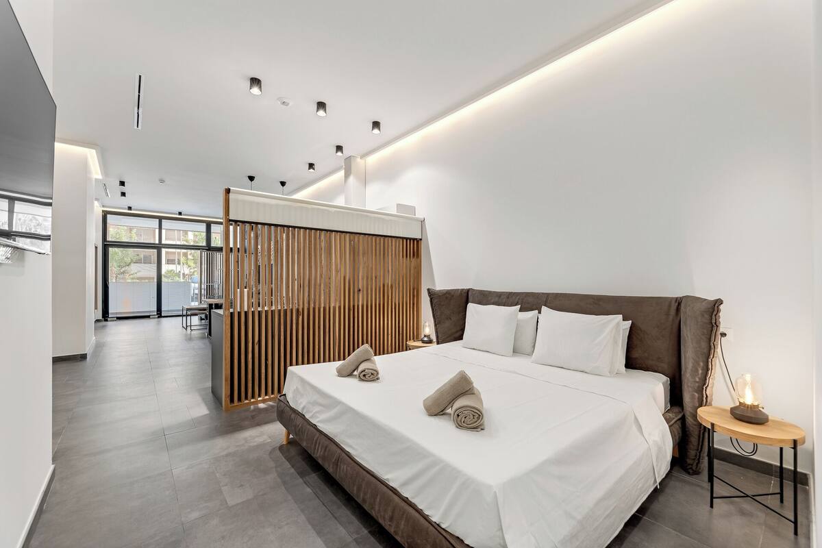 Un dormitorio moderno con una cama grande, un separador de madera y una mesita con una lámpara.