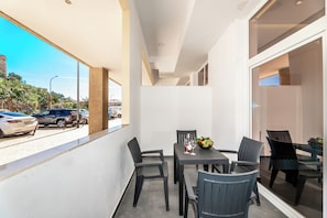 A balcony with a table set for two, chairs, and a view of parked cars and greenery outside.