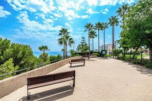 A paved walkway with benches, palm trees, and a view of the sea. - El Coloso Loft Eco Apartments (Benalmádena)