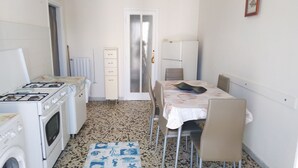 Una cocina compacta con estufa a gas, horno, microondas y lavadora. Hay una mesa de comedor con sillas y un tapete estampado en el suelo.