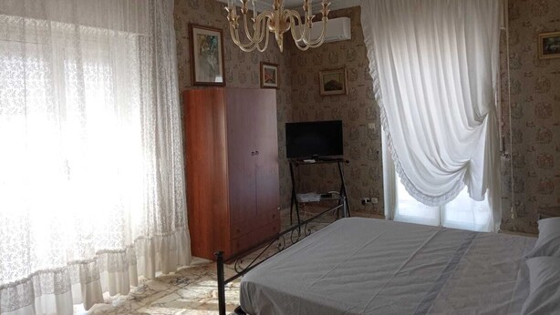 Un dormitorio con cama, armario de madera, televisor sobre un mueble bajo y una araña.