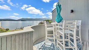 A balcony with white chairs and a teal umbrella, overlooking a lake with mountains in the distance. - Loft Condo with Stunning Lake Views (Moneta)