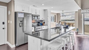 A modern kitchen with white cabinetry, stainless steel appliances, and a large island with bar stools. - Loft Condo with Stunning Lake Views (Moneta)
