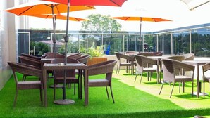 Un espace extérieur aménagé avec des chaises et des tables en osier, protégé par de grands parasols, et une balustrade en verre donnant sur un paysage verdoyant.