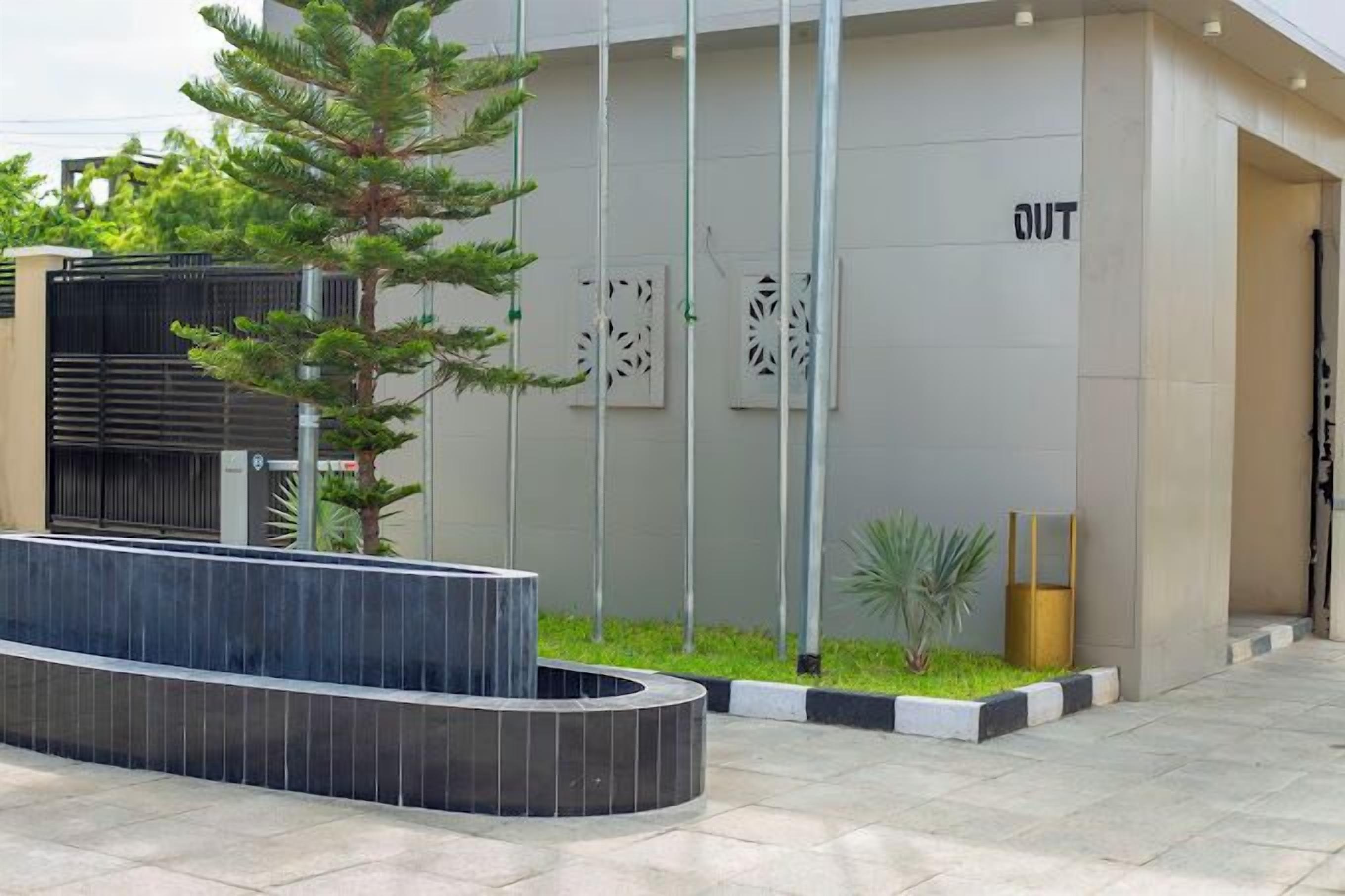 A modern building entrance with a curved black bench, a small garden area with plants, and a sign that reads "OUT".
