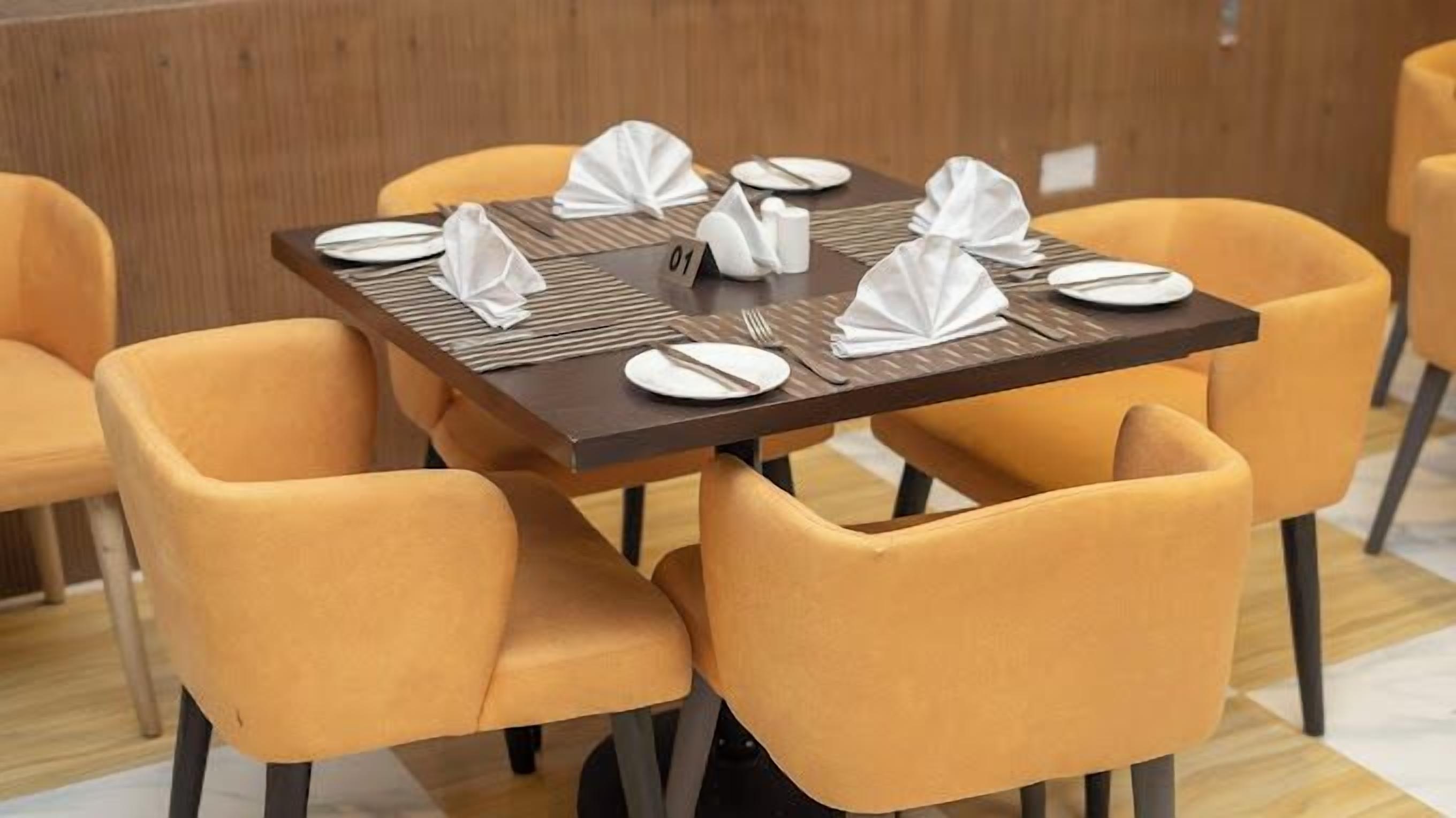 A dining area with a square table set for four, surrounded by four orange chairs.