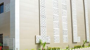 Une façade d’immeuble ornée de panneaux verticaux sur lesquels est inscrit du texte, un espace d’entrée pavé et un petit jardin avec différentes espèces de plantes.