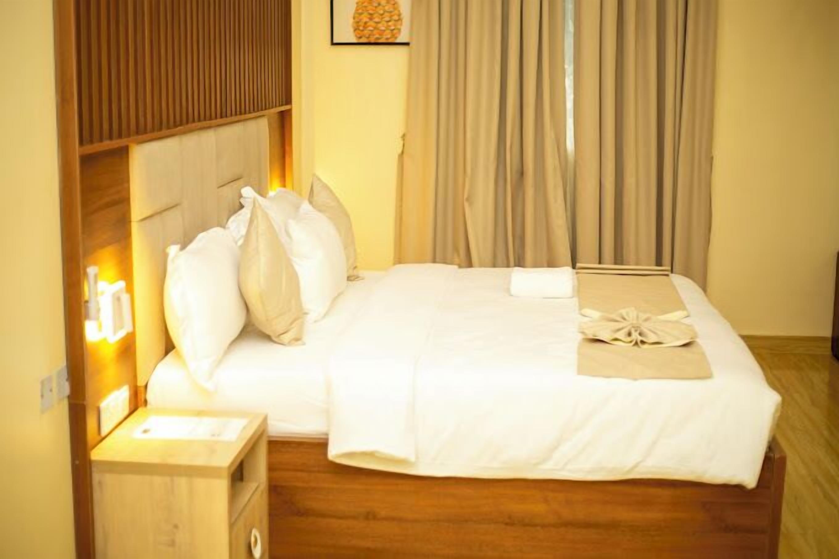 A neatly made bed with white linens and a decorative towel, a wooden headboard, a bedside table with a lamp, and a window with curtains.