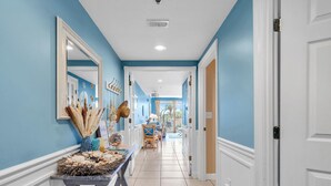A hallway with a tiled floor, a decorative table with various items, and a view into a dining area. - ⛱️ Sterling Shores 204 - Coastal Calm - Spacious Balcony ⛱️ (Destin)