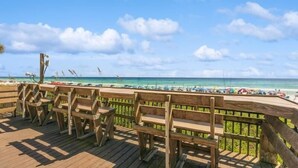 A wooden deck with benches overlooking a beach with umbrellas and people. - ⛱️ Sterling Shores 204 - Coastal Calm - Spacious Balcony ⛱️ (Destin)