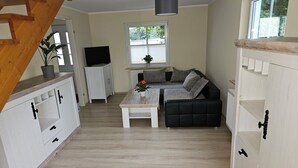 A modern living room with a sofa, coffee table, and TV. There is a staircase with a wooden railing leading to another level. - Vacation apartment Huschenbett in a rural idyll (Nessetal)