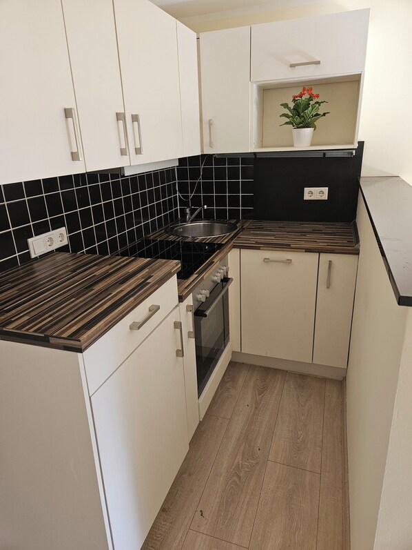 A compact kitchen with white cabinets, black tiled backsplash, wooden countertops, and a built-in oven.