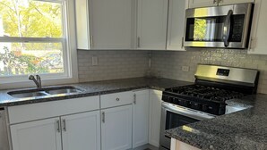 Une cuisine moderne avec des armoires blanches, un comptoir en granit, une cuisinière en acier inoxydable et un four à micro-ondes.