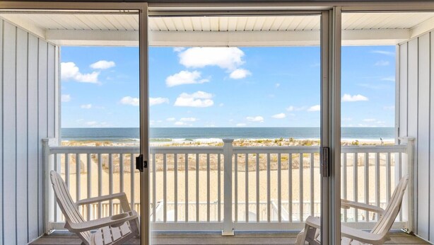 A balcony with two chairs, a wooden deck, and a view of the beach and ocean.
