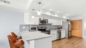 A modern kitchen with white cabinets, a granite countertop, stainless steel appliances, and a wooden floor.