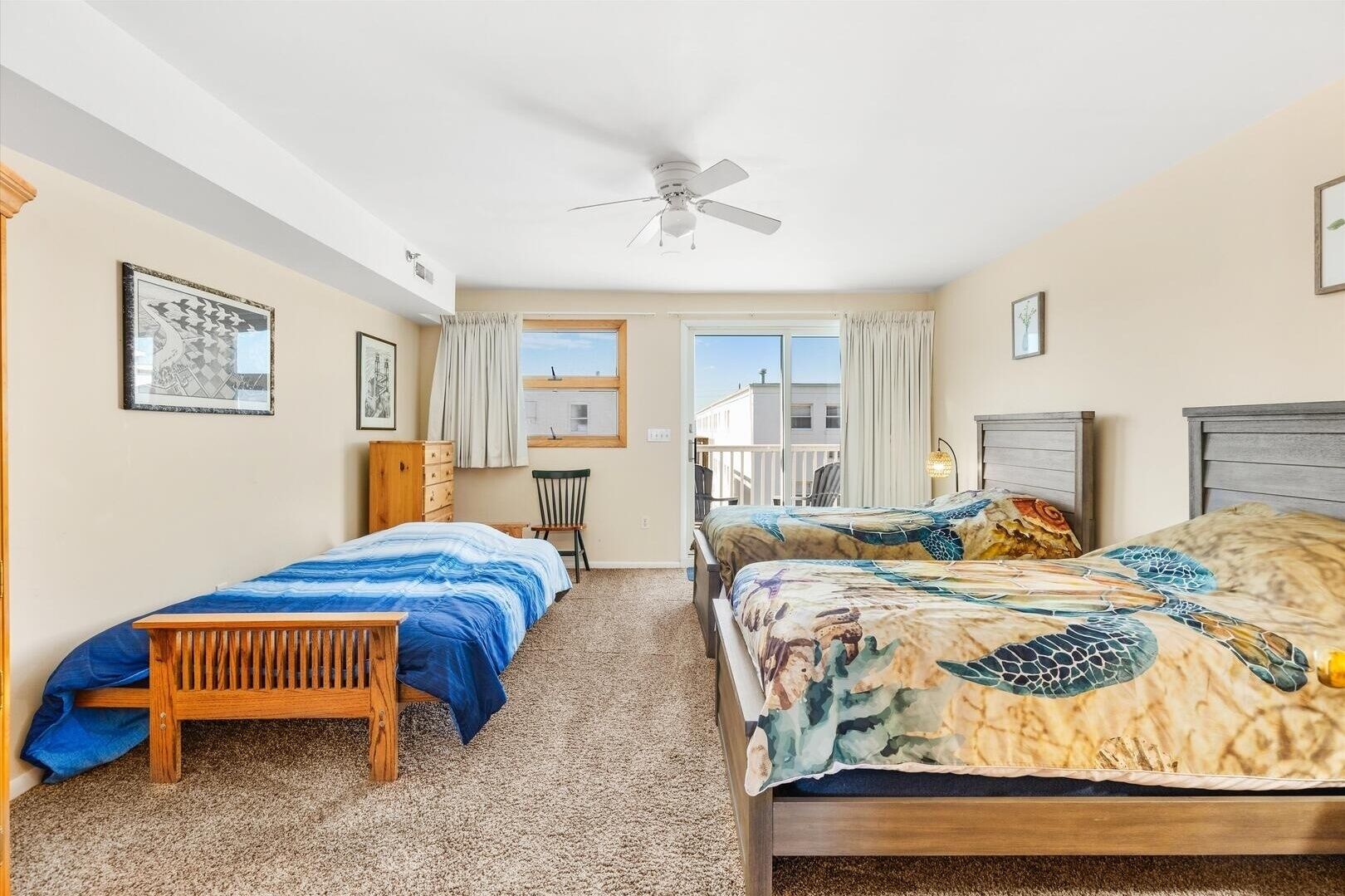A bedroom with two beds, a wooden bench, a ceiling fan, and a view of the outside.