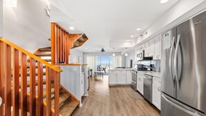A modern kitchen with a stainless steel refrigerator, wooden staircase, and a view to the living area.