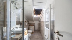 Une salle de bain moderne et compacte, dotée d’un puits de lumière, d’un lavabo, de toilettes et d’un espace douche.