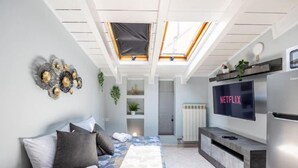 Une chambre moderne avec un puits de lumière, un lit avec une literie à motifs, une télévision et un banc intégré.