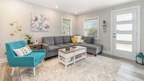Un salon moderne avec un fauteuil turquoise, un canapé d’angle gris et une table basse blanche.