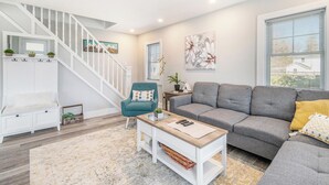 Un salon moderne avec un canapé gris, un fauteuil turquoise, une table basse blanche et un escalier doté de rampes blanches.