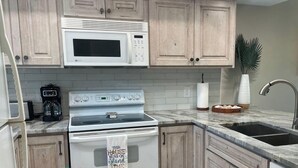 A kitchen with wooden cabinets, a white stove, a microwave, a sink, and a coffee maker. - Bocilla Island Club Unit C-13 (Bokeelia)