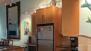 A kitchen with wooden cabinets, a stainless steel refrigerator, a coffee maker, and a large mirror. - Captains Harbor Island Hide Away (Bokeelia)