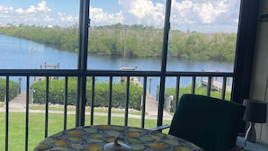 A balcony with a table covered in a fruit pattern, overlooking a body of water and greenery. - Captains Harbor Island Hide Away (Bokeelia)