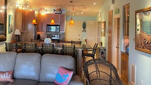 A spacious living area with a sofa, chairs, and a dining table. A kitchen is visible in the background with modern appliances. - Captains Harbor Island Hide Away (Bokeelia)
