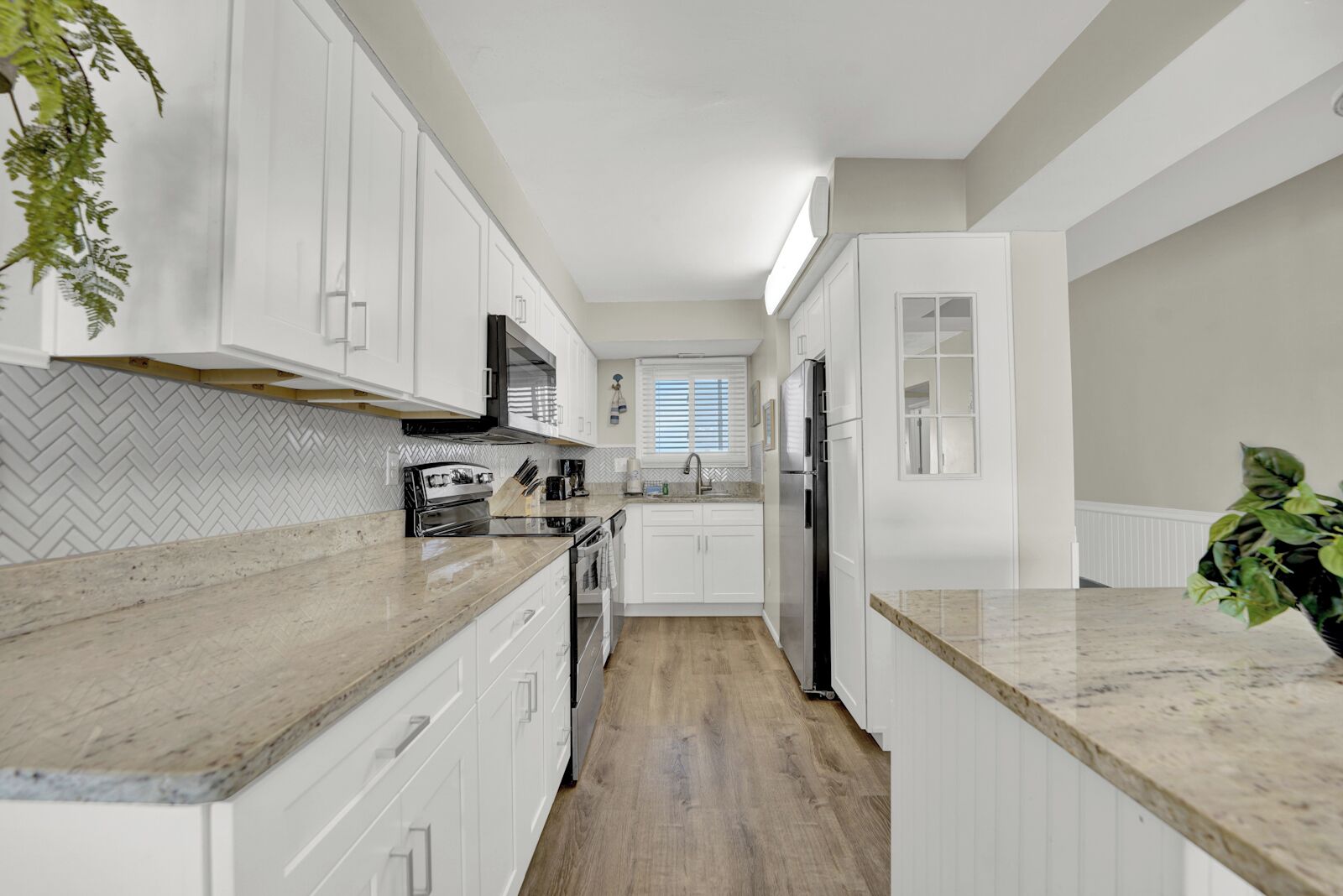 A modern kitchen with white cabinets, a herringbone-patterned backsplash, a stainless steel refrigerator, and a wooden floor.