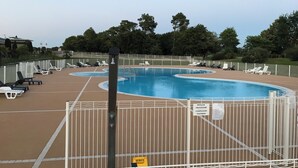 Ein Schwimmbecken mit mehreren Bahnen, umgeben von weißen Liegestühlen und einem eingezäunten Bereich.