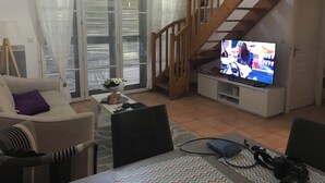Ein Wohnzimmer mit einer Couch, einem Couchtisch, einem Fernseher, einer Holztreppe und einem Balkon mit weißen Vorhängen.