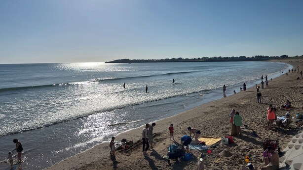 Ein Strand mit Menschen, die am Ufer entlanggehen, einem klaren Himmel und strahlender Sonne.