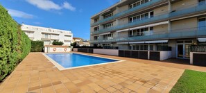 En boligbygning med swimmingpool, fliseterrasse og en velplejet have.