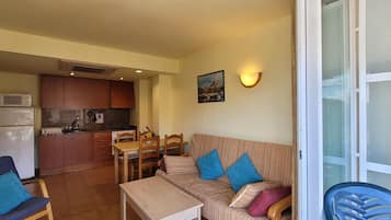 Un espacio habitable compacto con kitchenette, comedor y sofá con cojines.