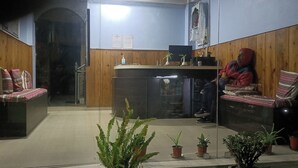 Un espace d’accueil comprenant un comptoir de réception en bois, un banc et plusieurs plantes en pot.
