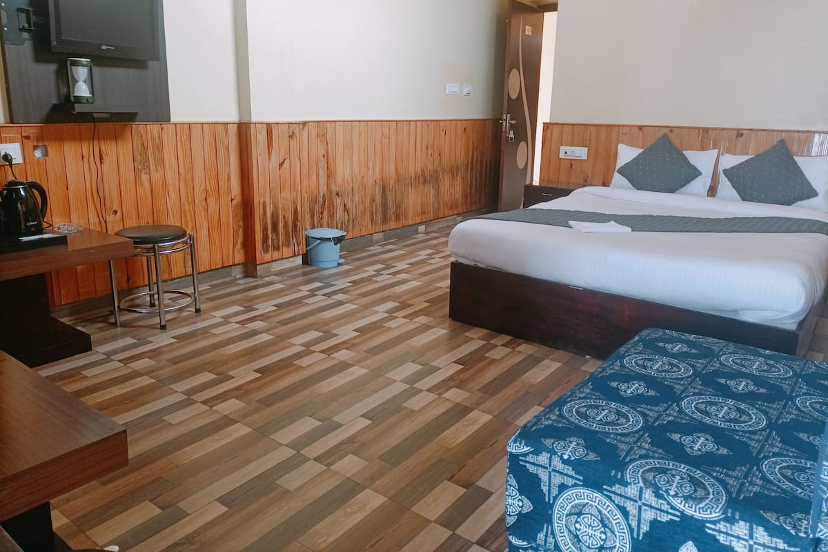 A hotel room with a bed, a desk, a chair, a coffee maker, and a trash can.