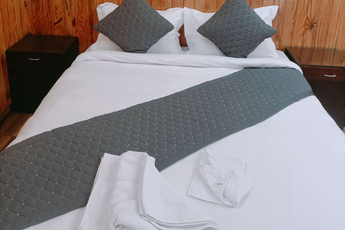 A neatly made bed with a grey quilt, white pillows, and a folded white towel.