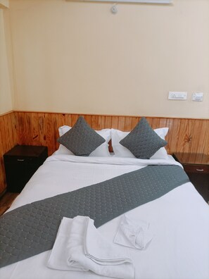 A neatly made bed with a grey quilt, white pillows, and a folded white towel.