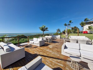 Een terras met buitenmeubilair, uitzicht op de oceaan en palmbomen.