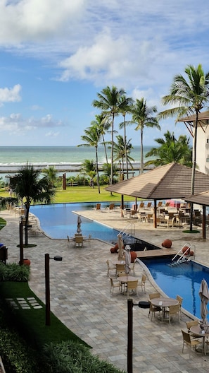 Ein Poolbereich eines Resorts mit Liegestühlen, Sonnenschirmen und Blick auf den Ozean.
