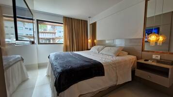 A modern hotel room with a large bed, a bedside table, a mirror, and a window with curtains.