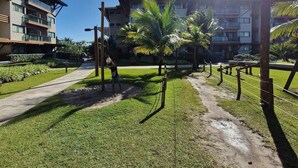 Un área verde con un sendero, palmeras y un edificio con varios balcones al fondo.