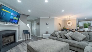 A modern living room with a fireplace, a grey sectional sofa, and a flat-screen TV mounted on the wall. - Charming 3-bedroom house with AC, WiFi in terrific Lithia Springs (Lithia Springs)